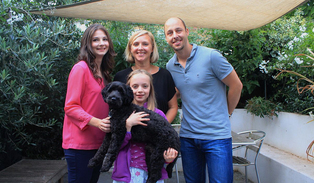 Three adults and a child. The child is holding a medium sized, black, curly-haired dog.