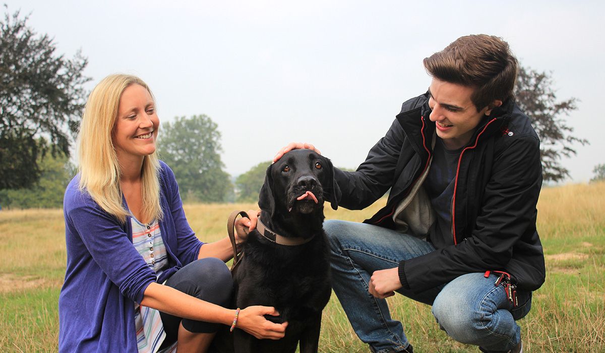 Oso, the black Lab is flanked by two people who are paying attention to him. 
